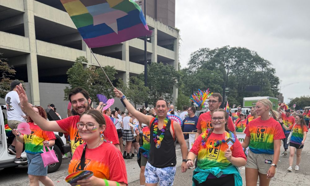 several people wave and smile and they march through the street during the Cincinnati Pride Parade
