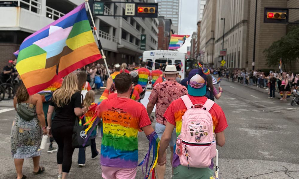 Two men holding hands and one holding a Jewish pride flag, marching through the street during the pride parade