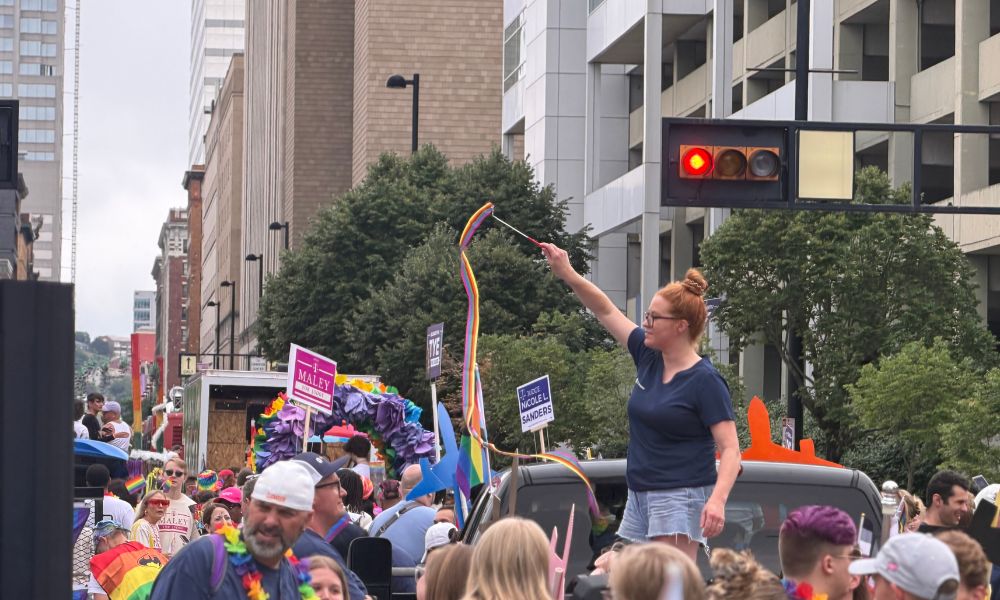 A woman standing on a truck bed twirling a rainbow ribbon